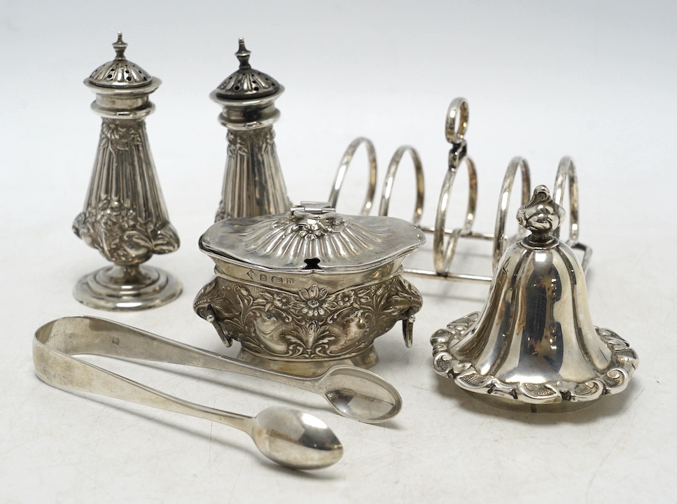 Sundry silver including a pair of Edwardian pepperettes, a five bar toast rack, a mustard pot (a.f.), a pair of sugar tongs and a cover. Condition - poor to fair